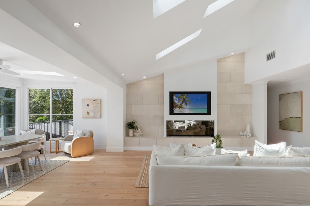 Bright modern living room with white walls, skylights, large windows, and a TV above the fireplace