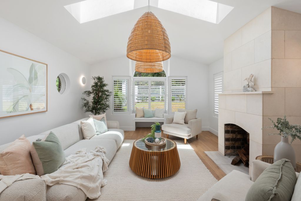 Bright white living room with skylights, woven pendant light, cream sofas, and striped coffee table.