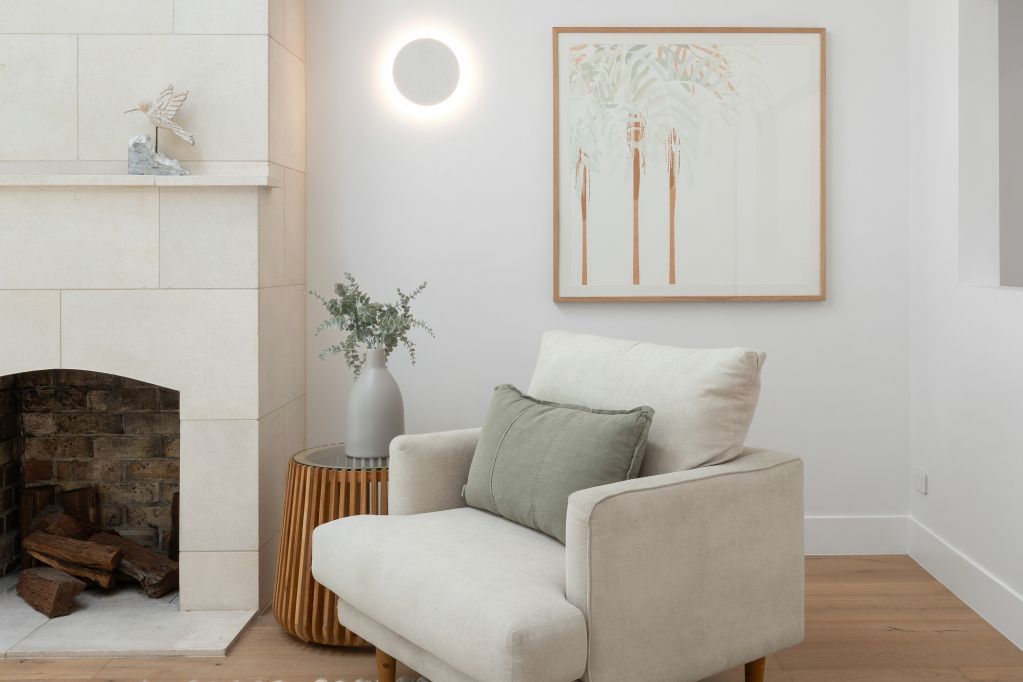 Minimalist living room with white armchair, fireplace, wall art, and soft neutral decor