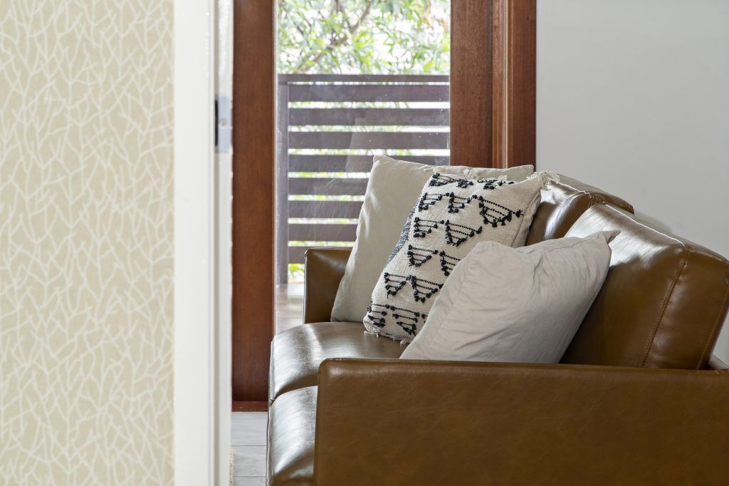 A living room with a brown leather couch and white pillows.