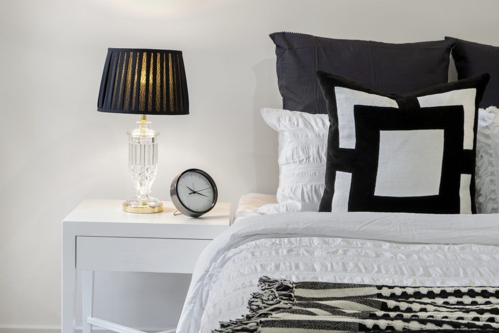 A bedroom with a bed , nightstand , lamp and clock.