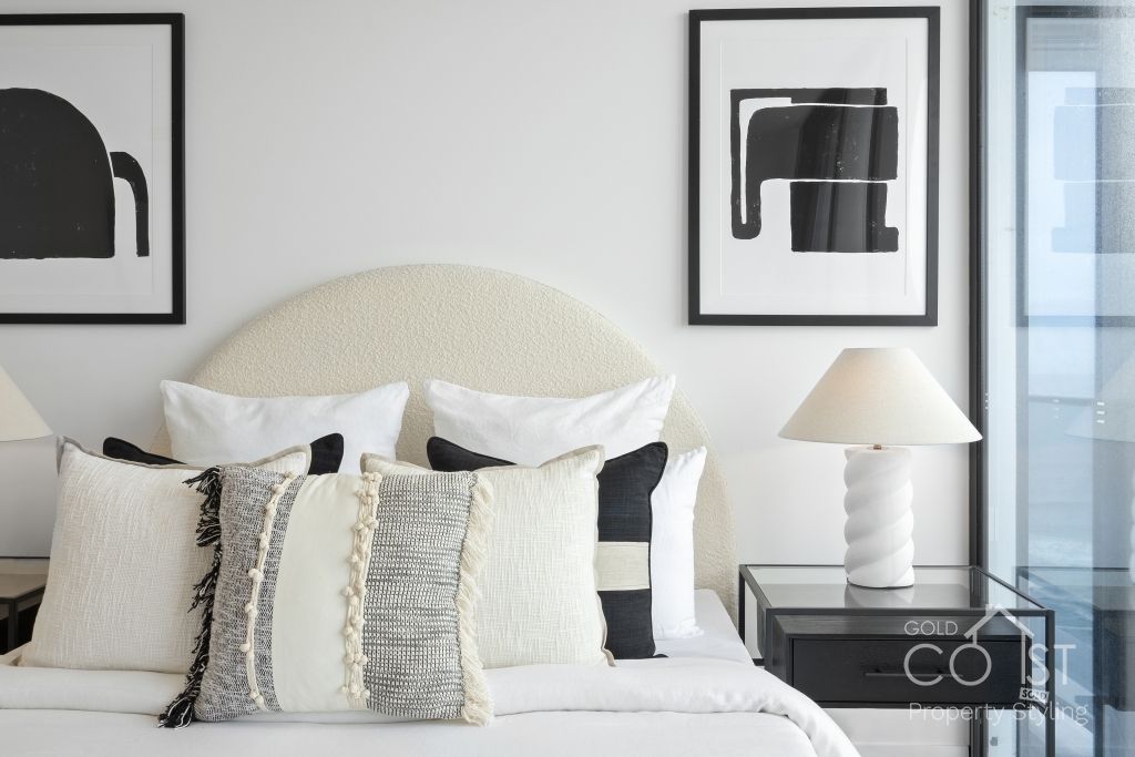 A bedroom with a bed , lamps , pillows and paintings on the wall.