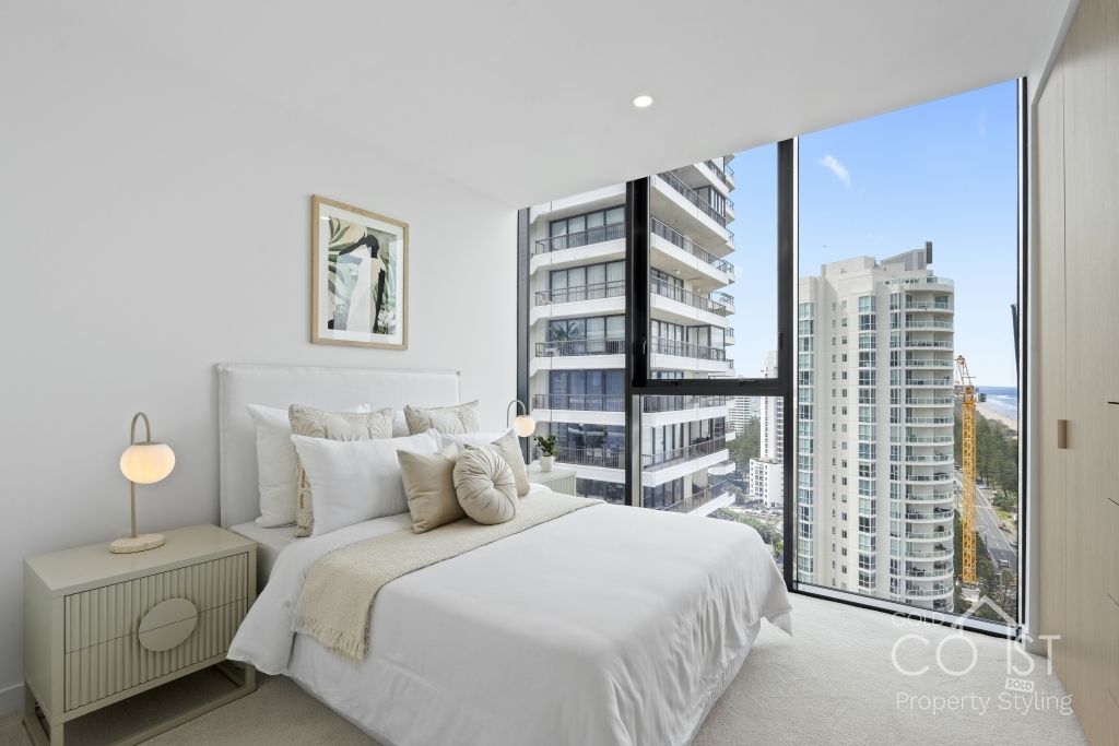 A bedroom with a large bed and a large window with a view of a city.