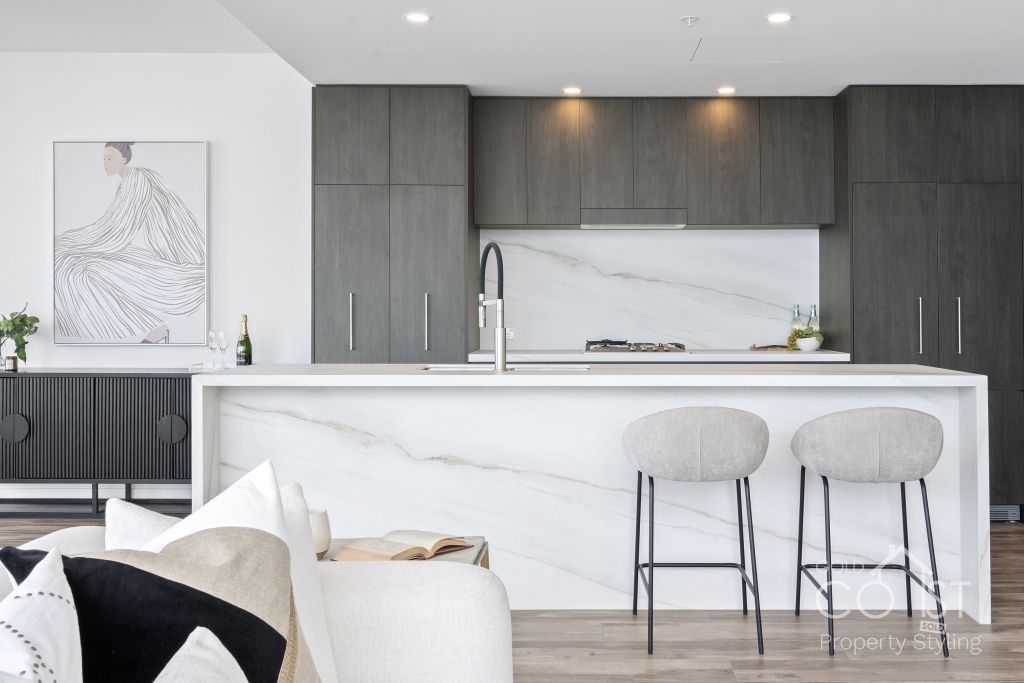A kitchen with a large island and stools in a living room.