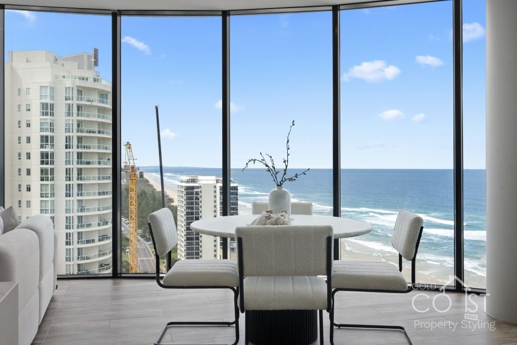 A living room with a dining table and chairs and a view of the ocean.