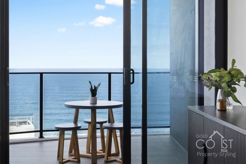 A balcony with a table and stools overlooking the ocean.