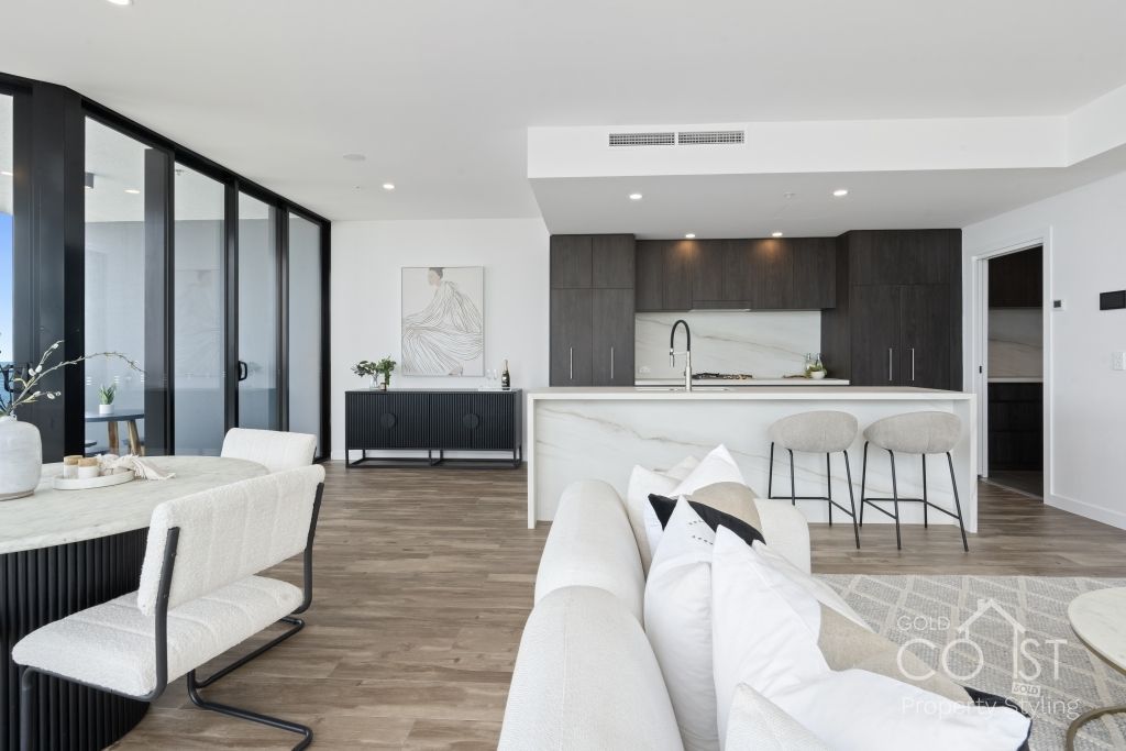 A living room with a couch , chairs , a table and a kitchen.