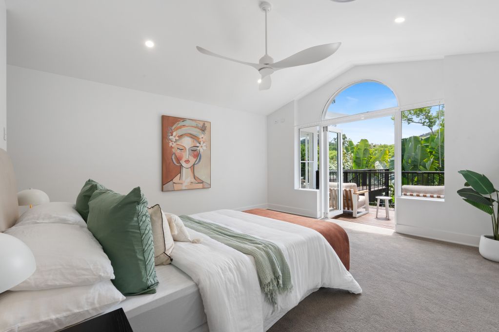 Bright white bedroom with bed, green pillows, and open doors to a sunlit balcony.