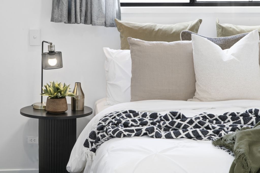 A bedroom with a bed , nightstand , lamp and window.