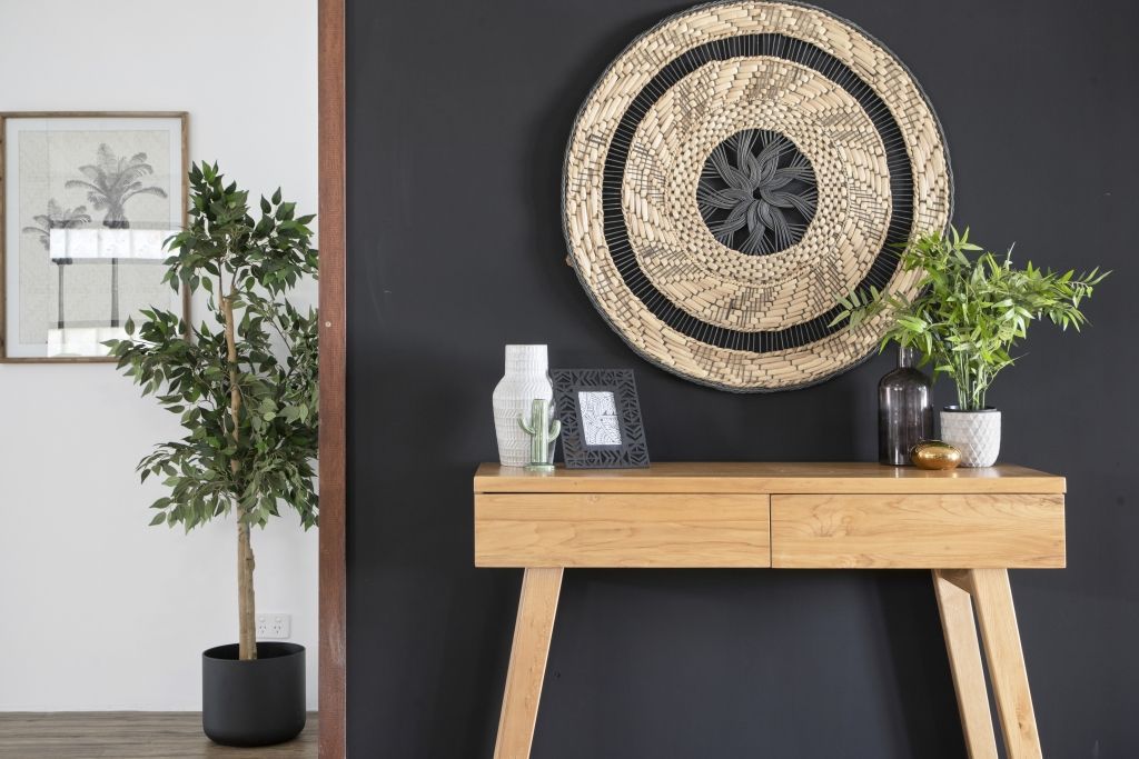 A wooden table with a clock on it is in a hallway next to a potted plant.
