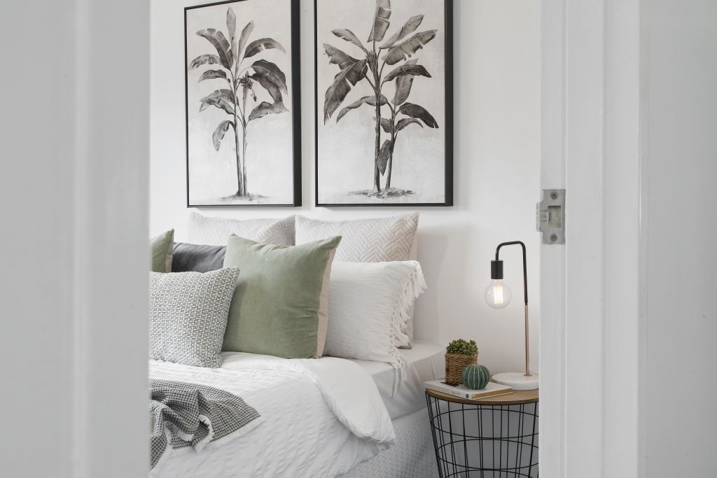 A bedroom with a bed , nightstand , lamp and paintings on the wall.