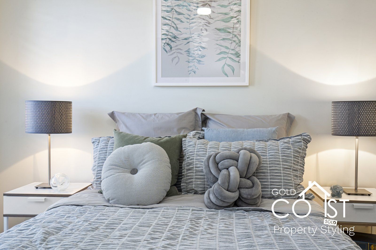 A bedroom with a bed , pillows , lamps and a picture on the wall.