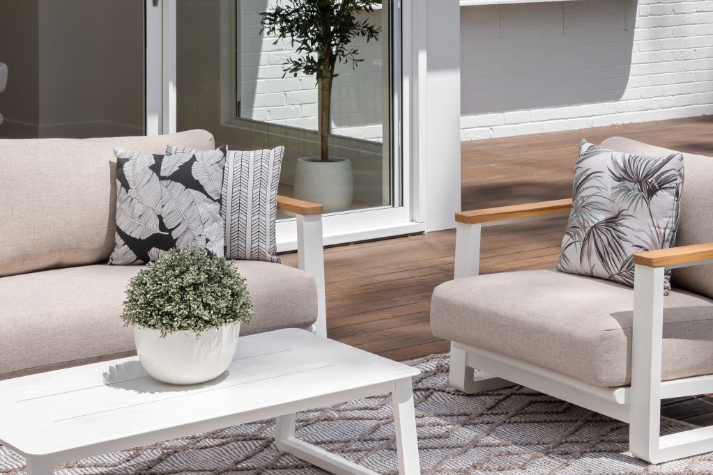 Modern patio with white furniture, gray patterned cushions, and a potted plant beside sliding glass doors