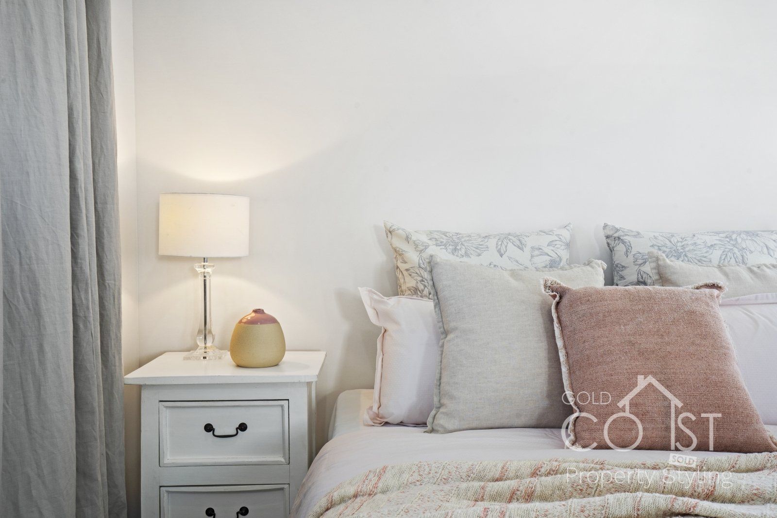 A bedroom with a bed , nightstand , lamp and pillows.