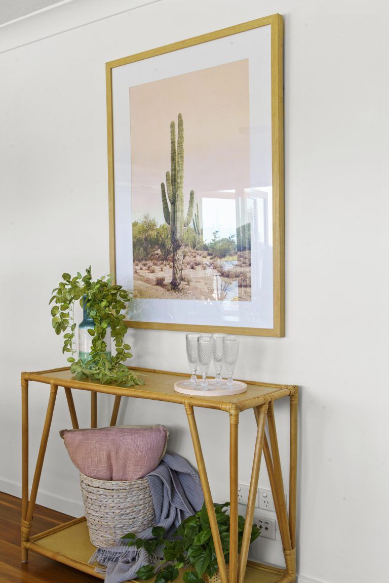A picture of a cactus is hanging on a wall above a wooden table.