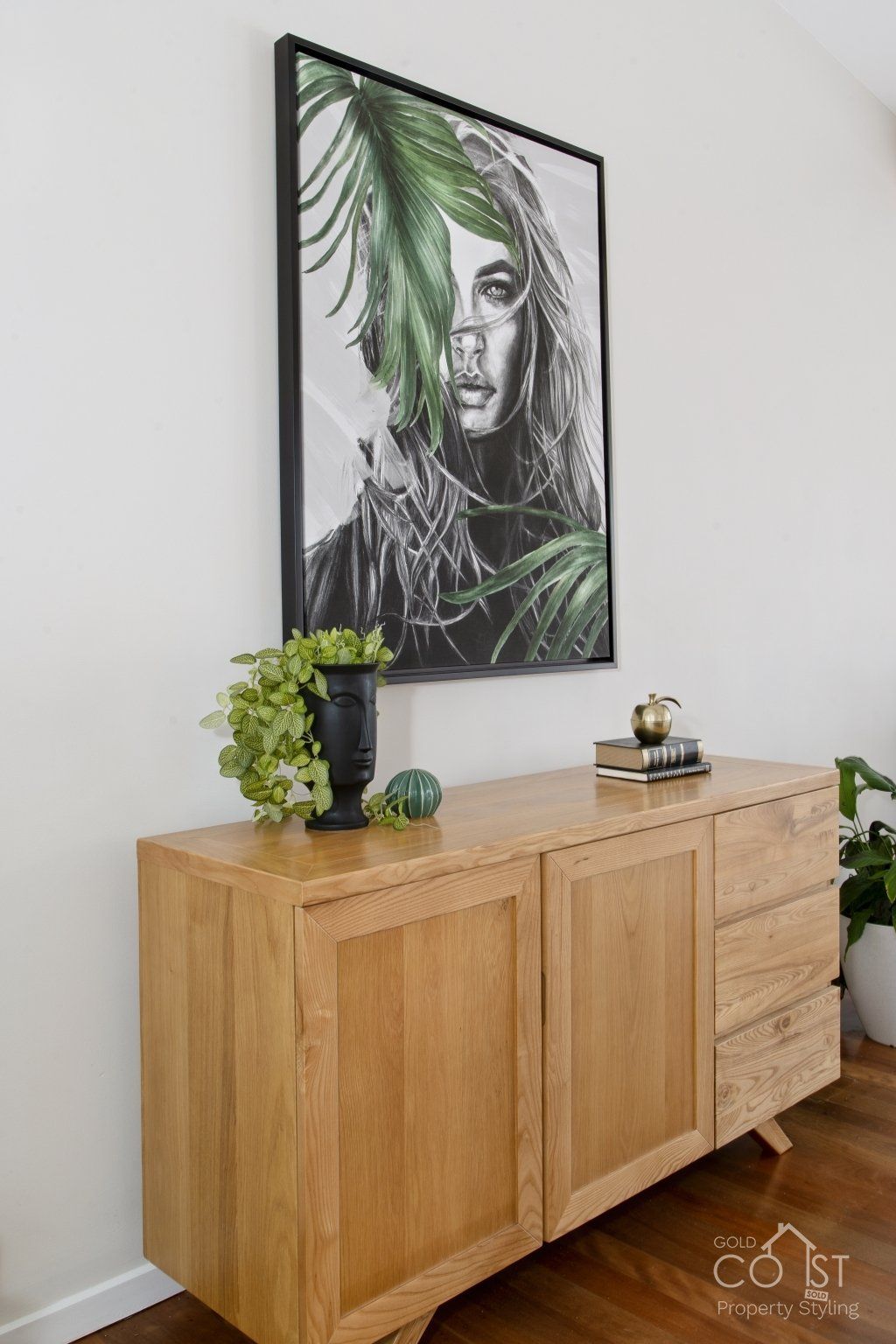 A wooden dresser with a painting on the wall above it.