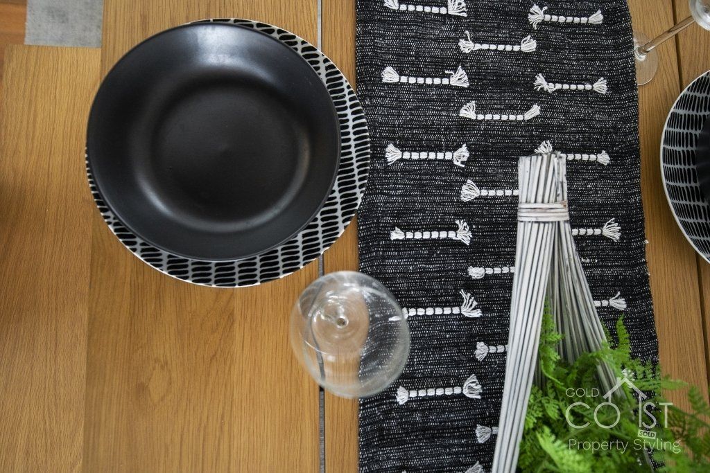 A wooden table with black and white plates and a black and white table runner.