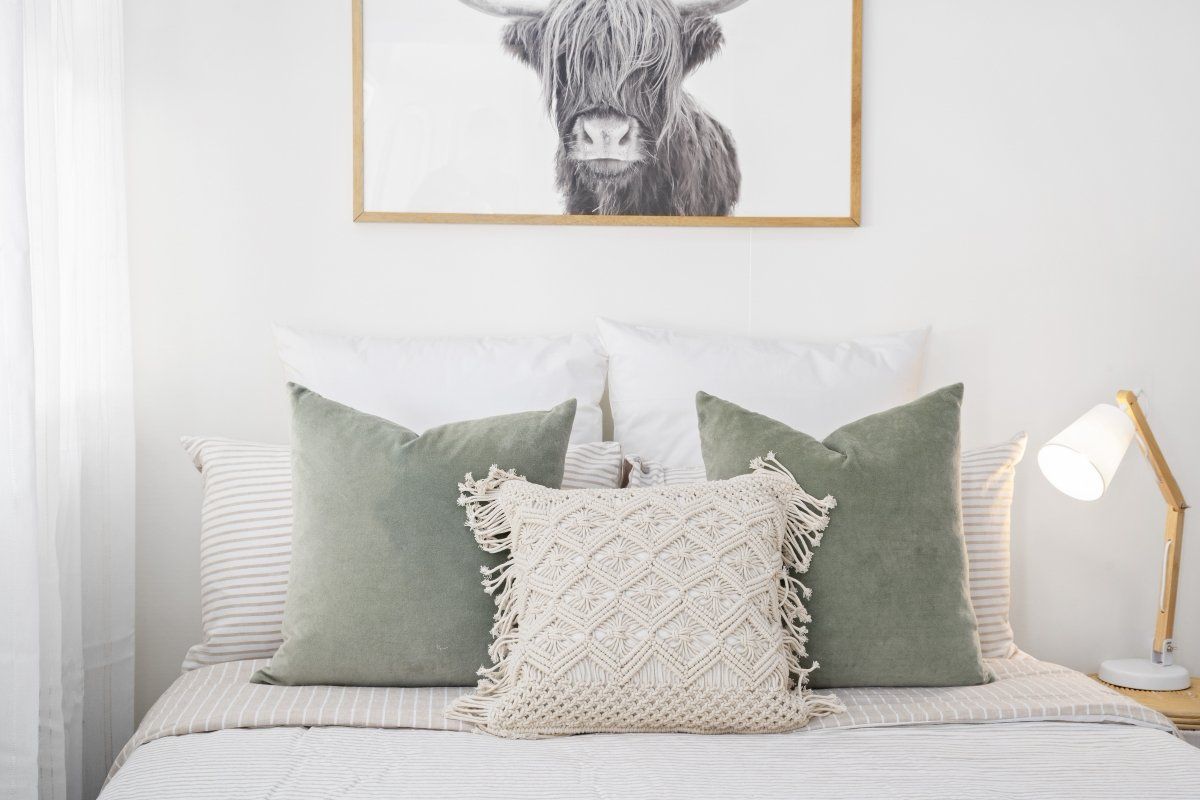 A bed with pillows and a picture of a cow on the wall above it.