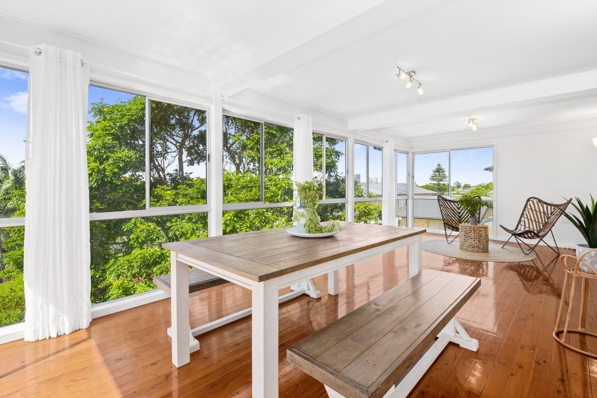 A living room with a table and bench and lots of windows.