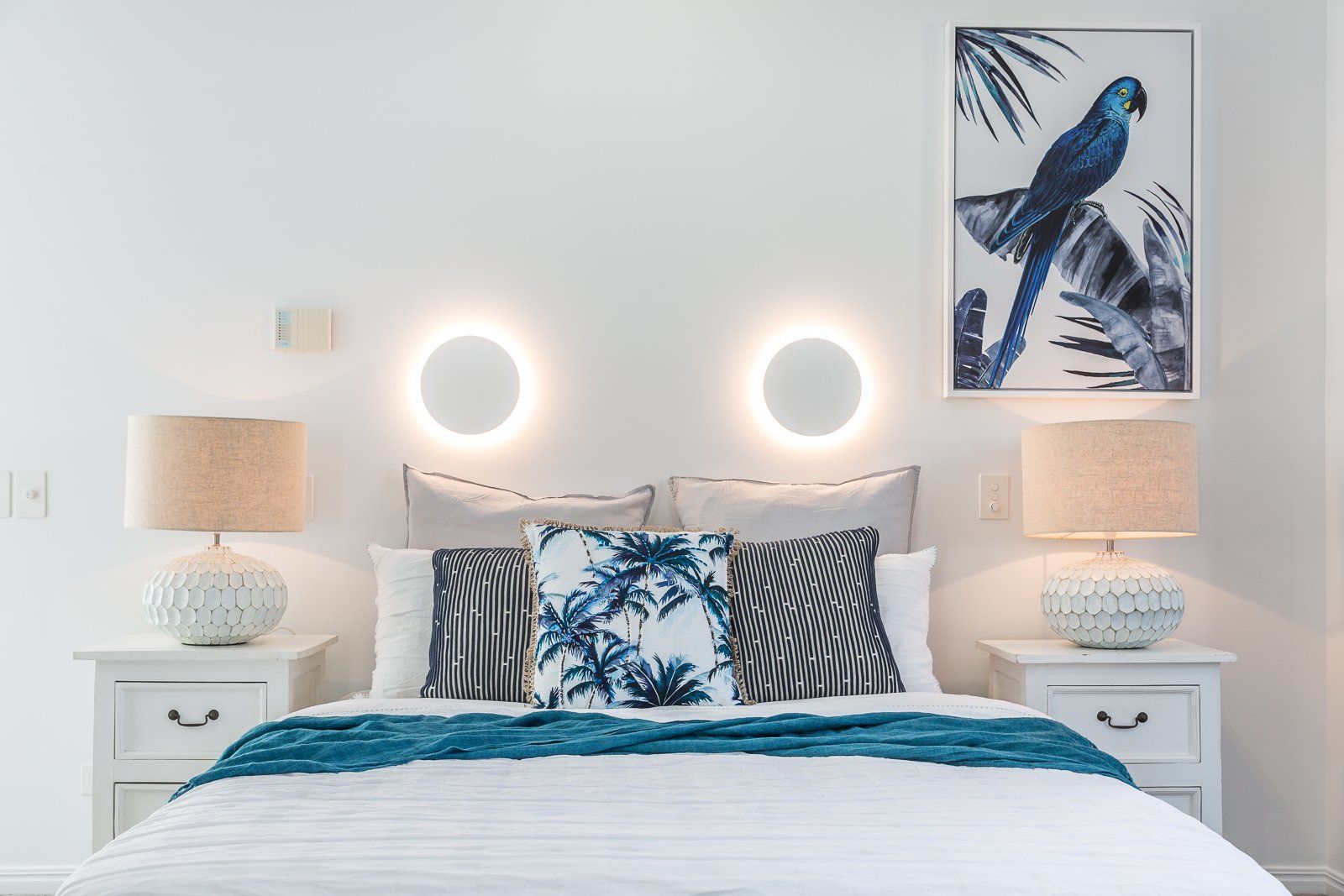 A bedroom with a bed , two nightstands , two lamps and two paintings on the wall.