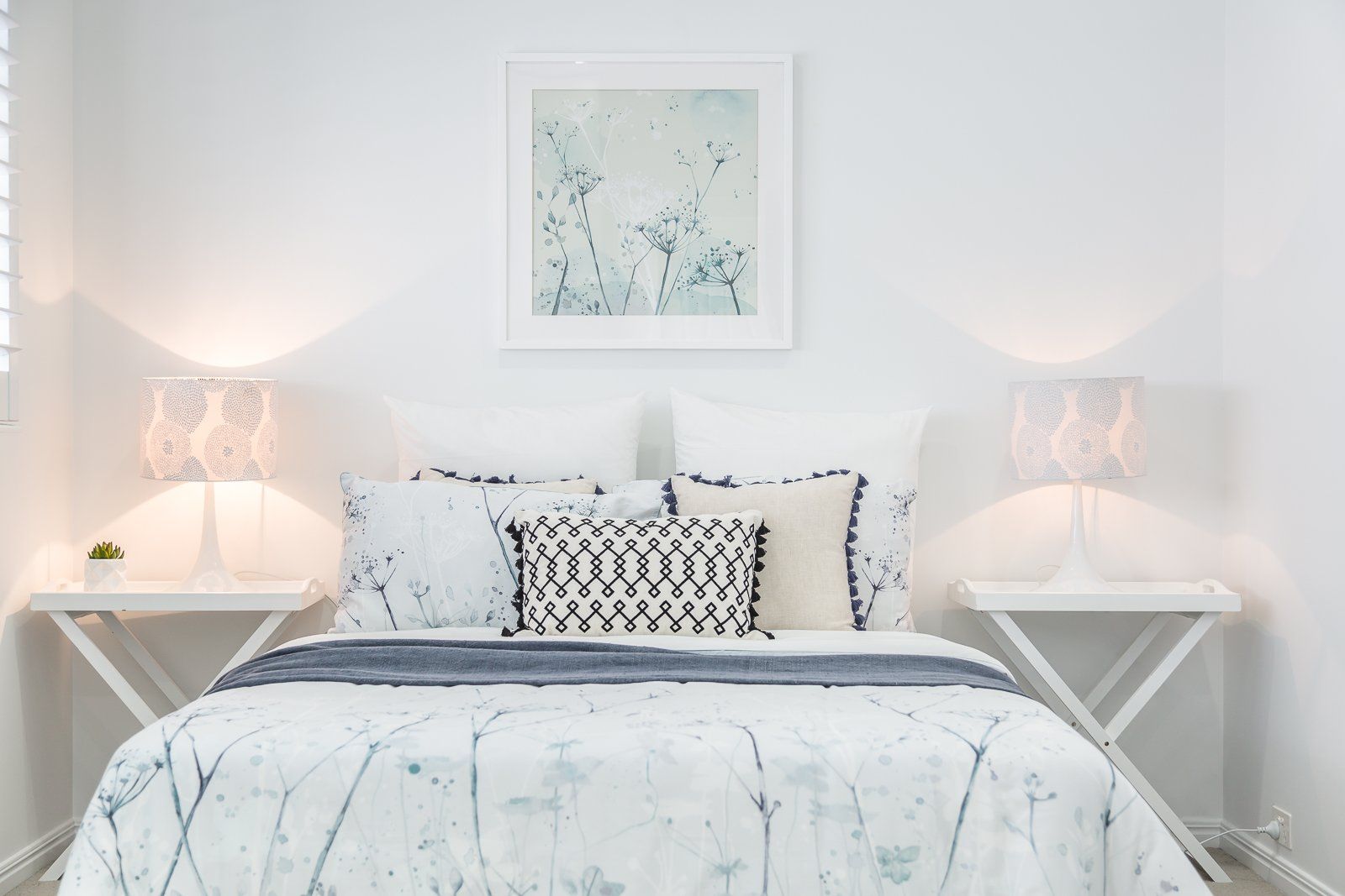 A bedroom with a bed , nightstands , lamps and a picture on the wall.