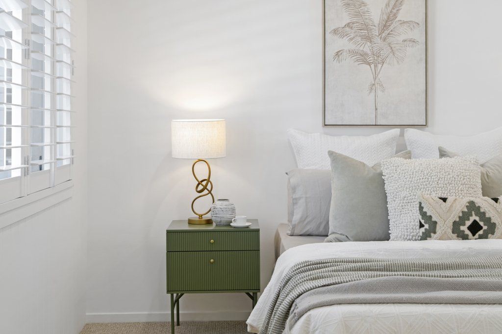 A bedroom with a bed , nightstand , lamp and painting on the wall.