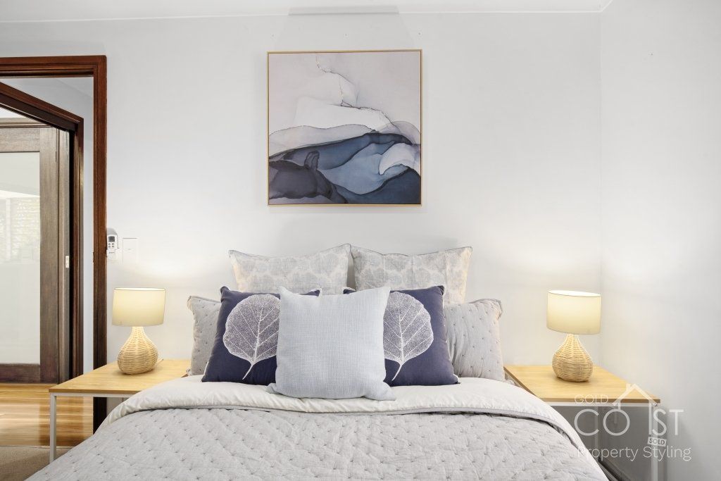 A bedroom with a bed , lamps , pillows and a painting on the wall.