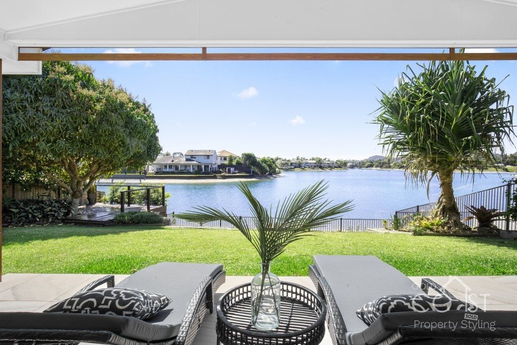 A view of a lake from a patio with lounge chairs and a table.