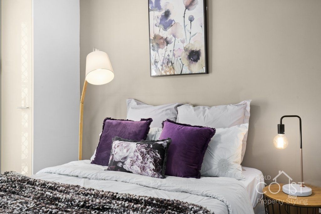 A bed with purple pillows and a lamp in a bedroom.