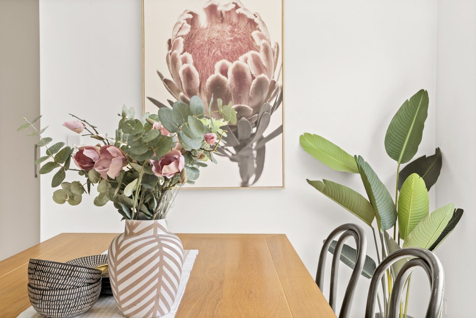 A dining room table with a vase of flowers and a painting on the wall.