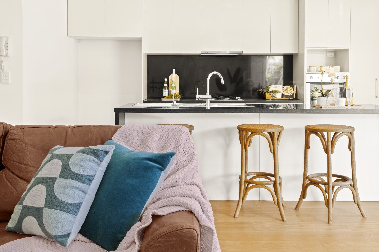 A living room with a couch and stools and a kitchen in the background.