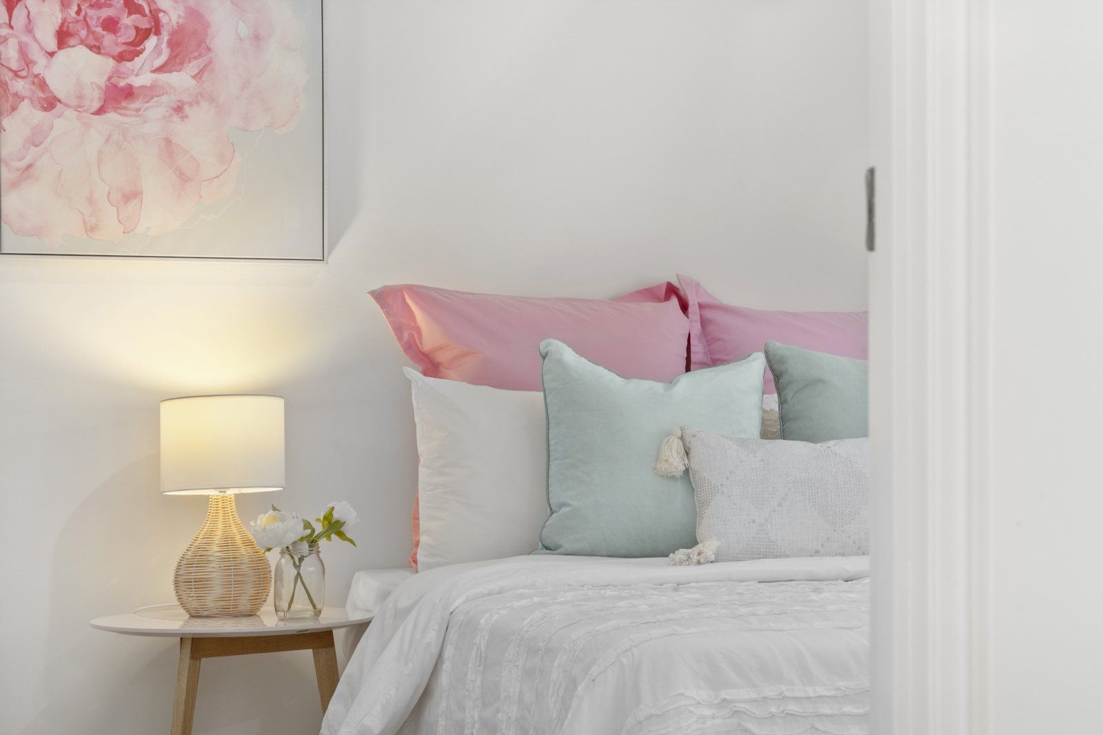 A bedroom with a bed , nightstand , lamp and painting on the wall.