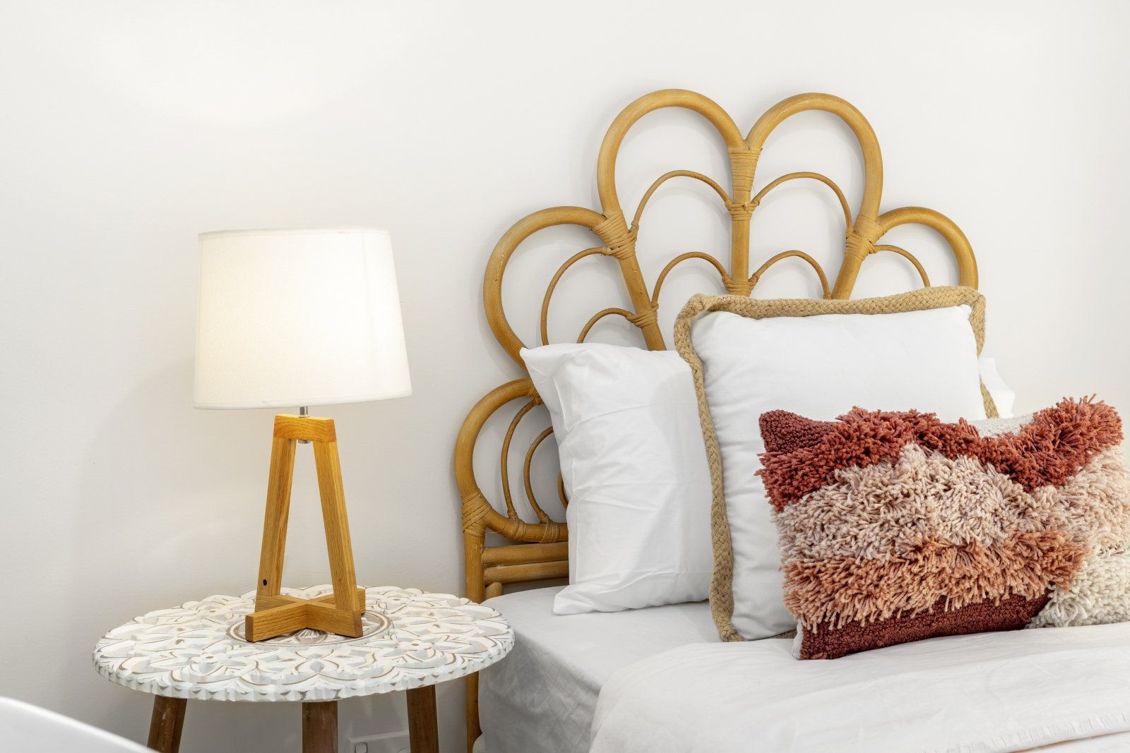 A bedroom with a bed , nightstand , lamp and wicker headboard.
