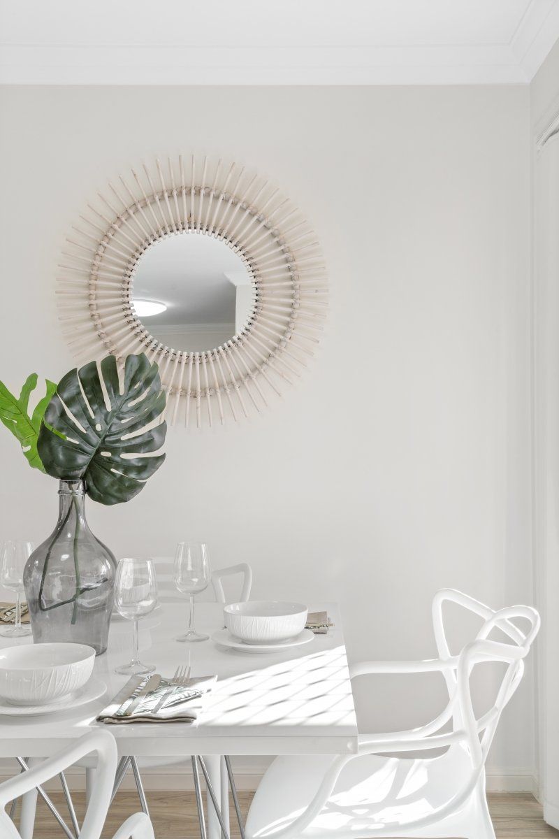 A dining room with a table and chairs and a mirror on the wall.