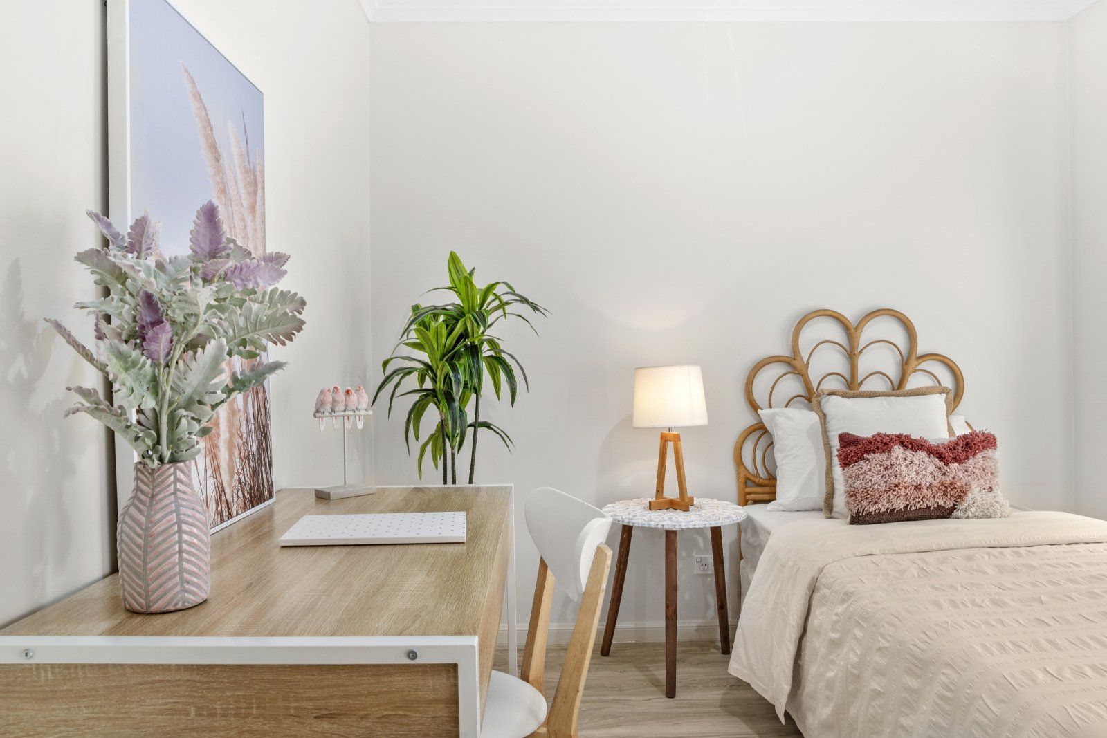 A bedroom with a bed , desk , lamp and painting on the wall.