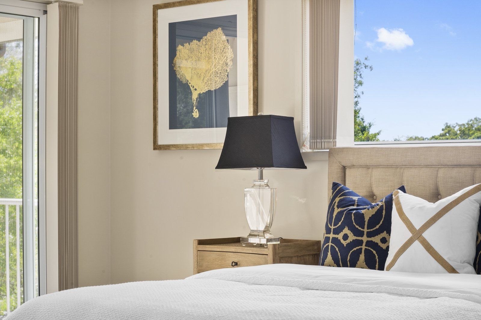 A bedroom with a bed , nightstand , lamp and window.