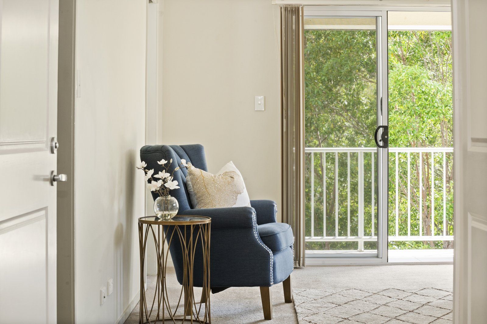 A living room with a chair , table and sliding glass doors leading to a balcony.