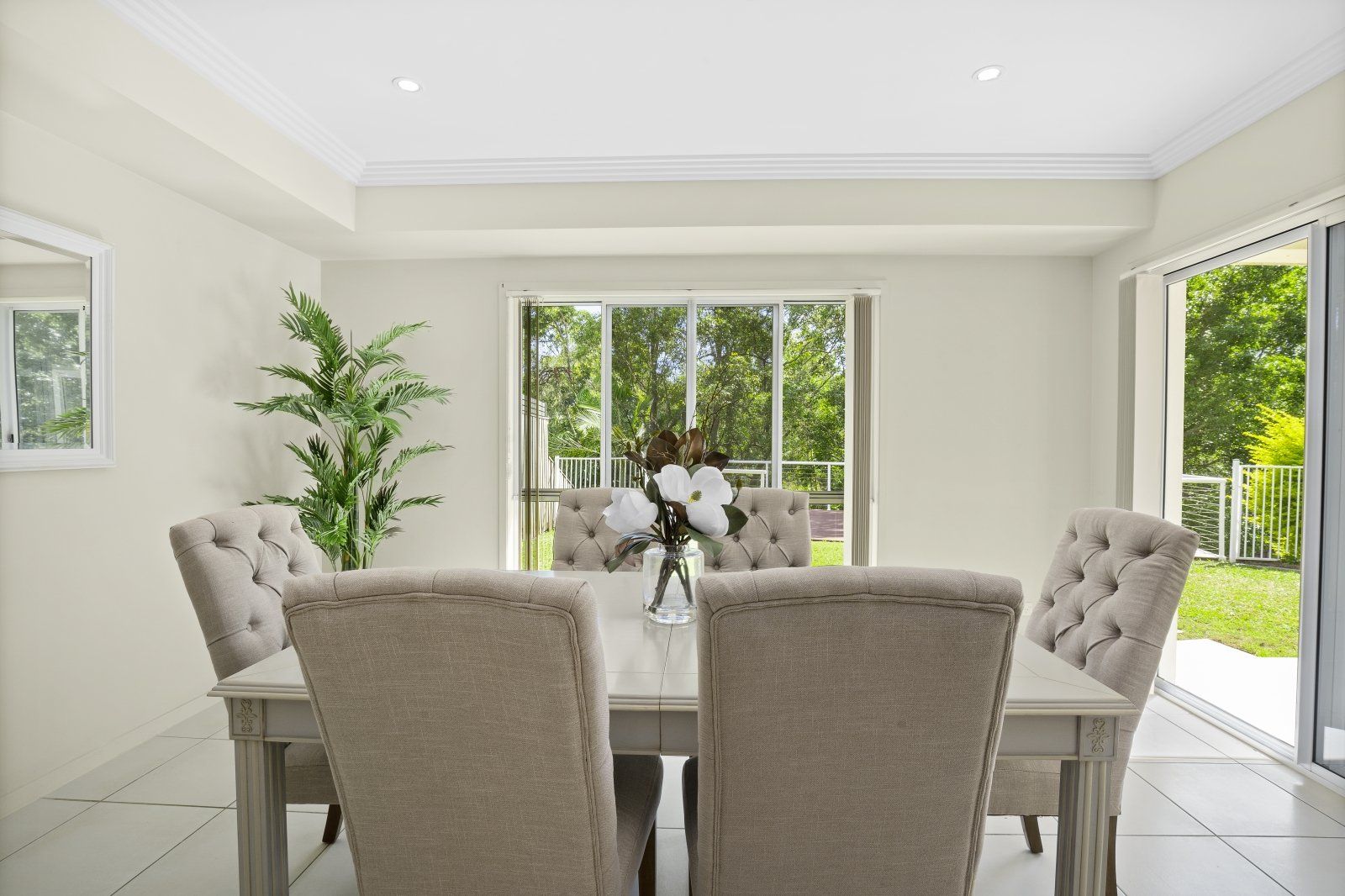 A dining room with a table and chairs and a vase of flowers on the table.