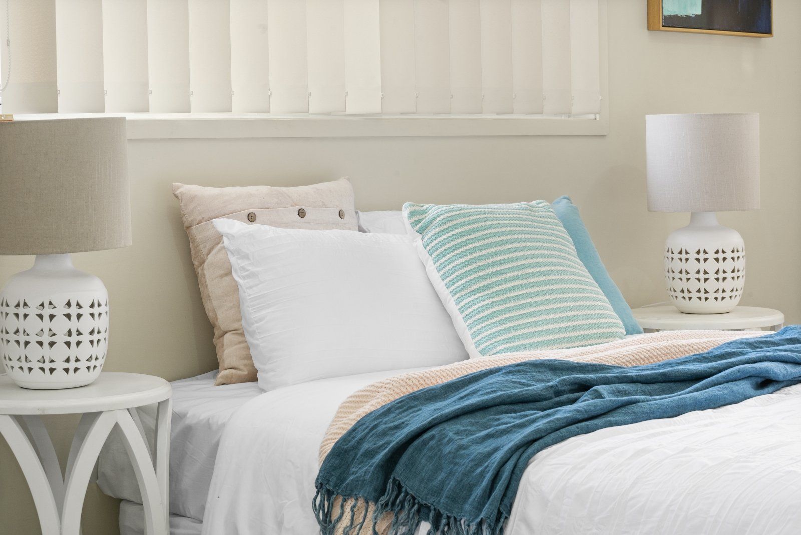 A bed with white sheets , pillows , a blanket and a lamp in a bedroom.