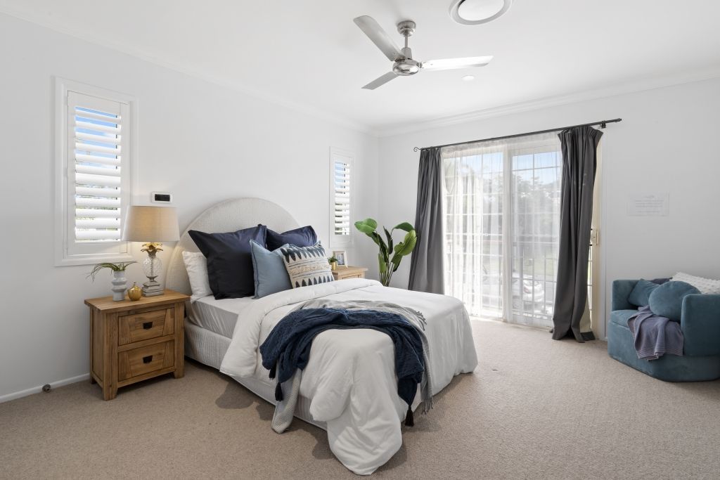 A bedroom with a bed , nightstand , ceiling fan and sliding glass doors.