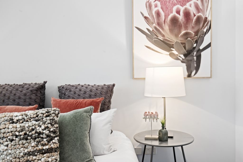 A bedroom with a bed , nightstand , lamp and a painting of a flower on the wall.