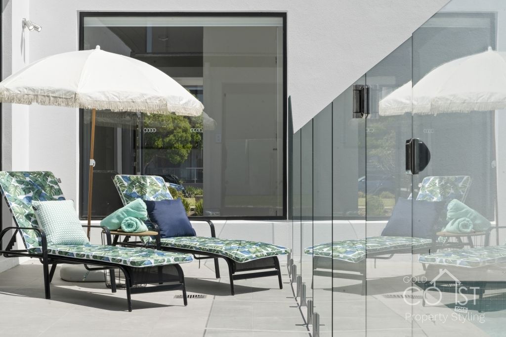 A patio with lounge chairs and umbrellas and a glass fence.