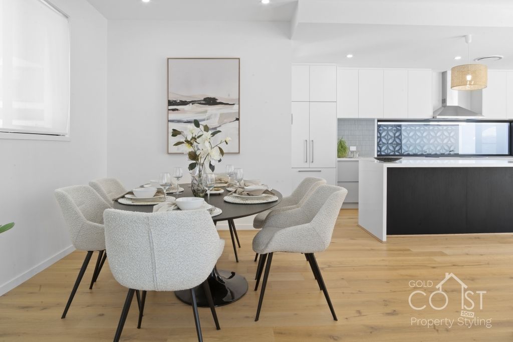 A dining room with a table and chairs and a kitchen in the background.