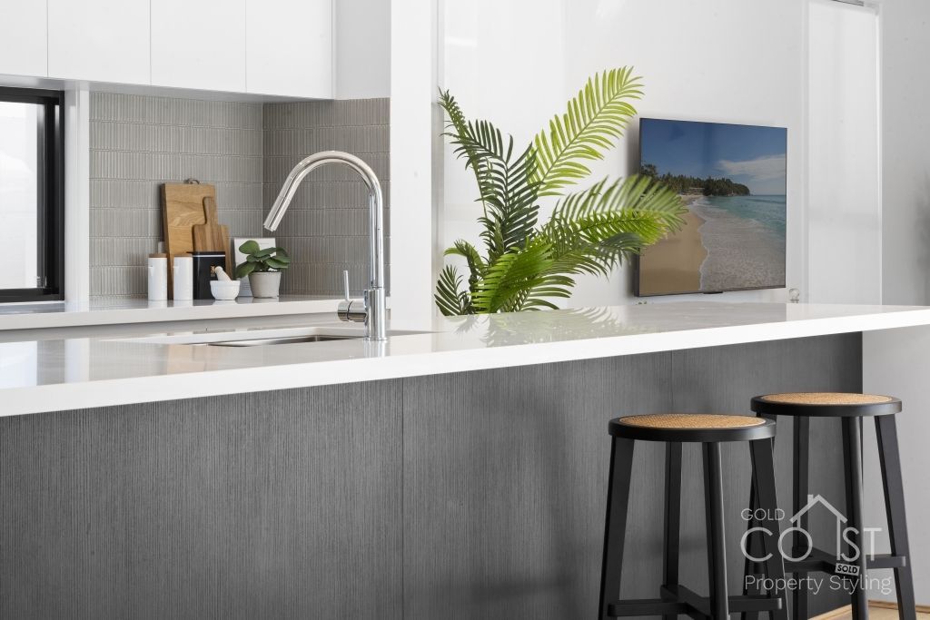 A kitchen with a sink , stools , and a painting on the wall.