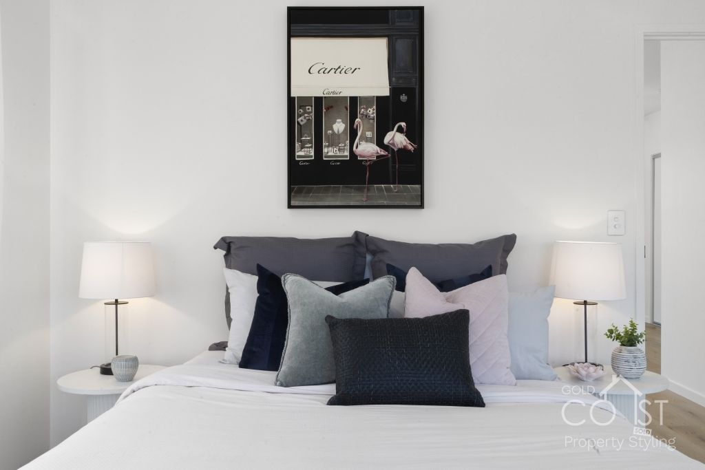 A bedroom with a bed , lamps , pillows and a painting on the wall.