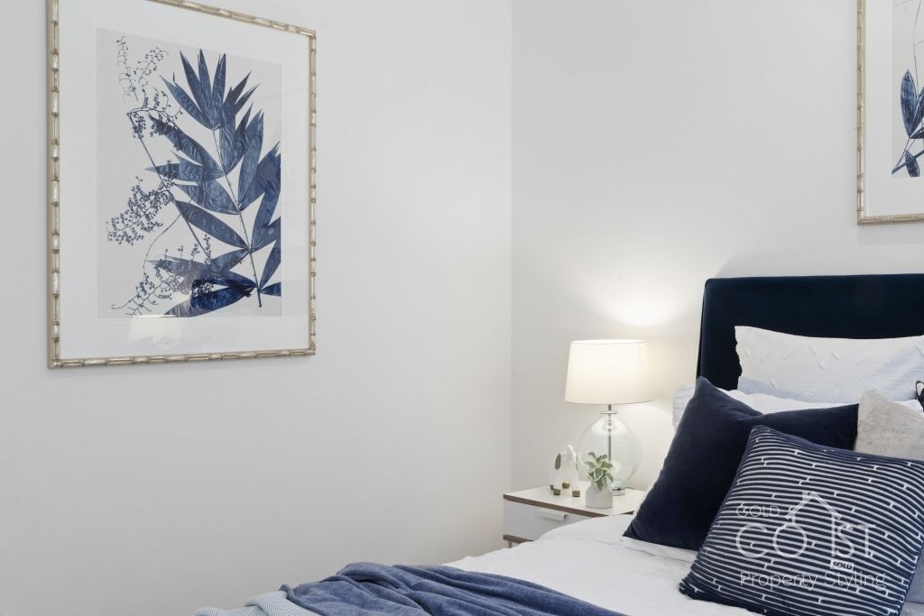 A bedroom with a bed , nightstand , lamp and painting on the wall.