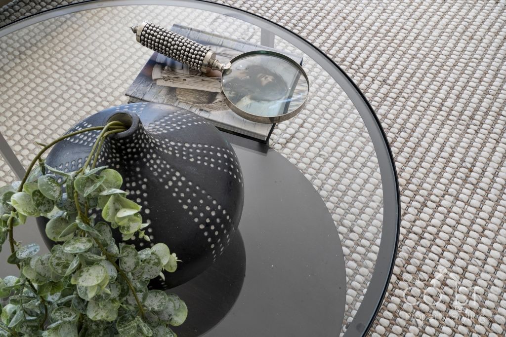 A glass coffee table with a vase and magnifying glass on it.