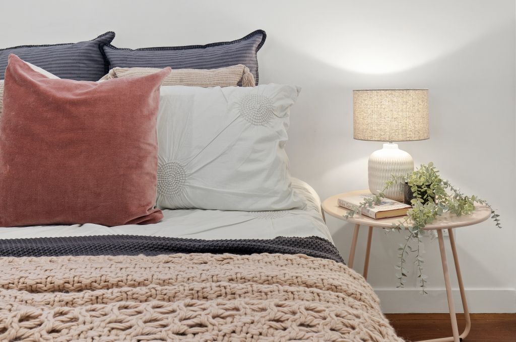 A bedroom with a bed , nightstand , lamp and pillows.