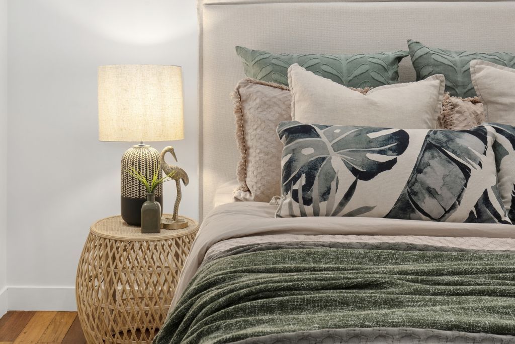 A bedroom with a bed , nightstand , lamp and pillows.