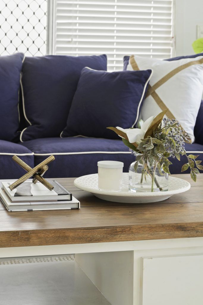 A living room with a blue couch and a wooden coffee table with a vase of flowers on it.